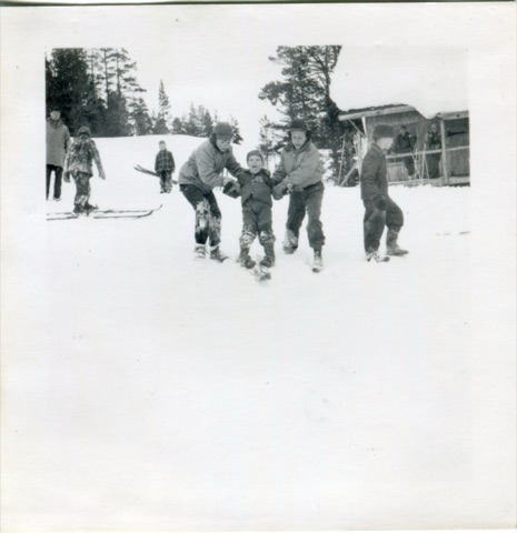 1950 Older kids guiding younger kid learning how to ski near lodge
