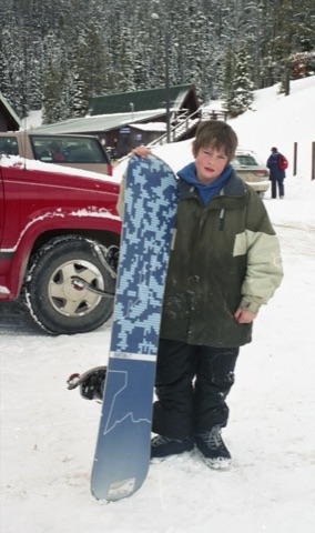 2000s Jared Burtonwith snowbaord near lodge.