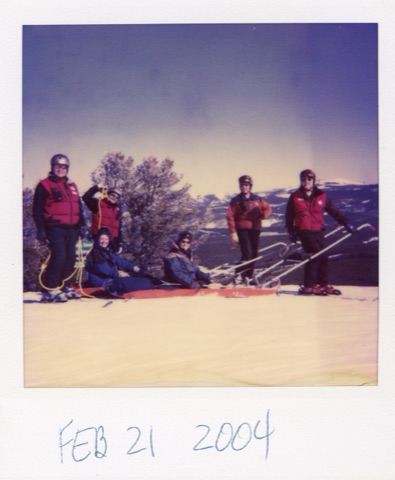 A Polaroid of patrollers in red vests beside a red rescue toboggan with two people riding in it