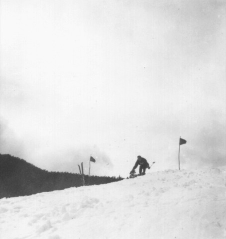 1940s A skier reaching for the snow by a gate